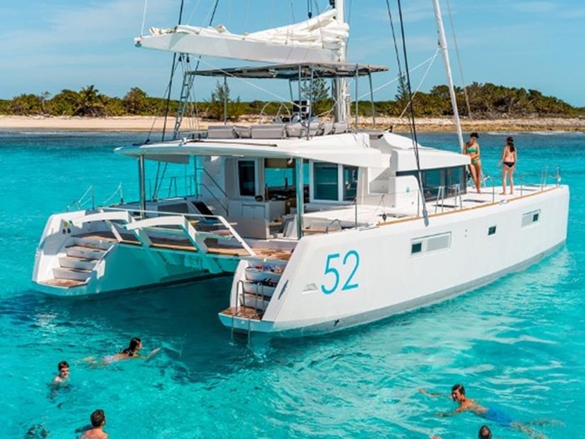 Sailing catamaran anchored in turquoise water with swimmers in the water off the stern