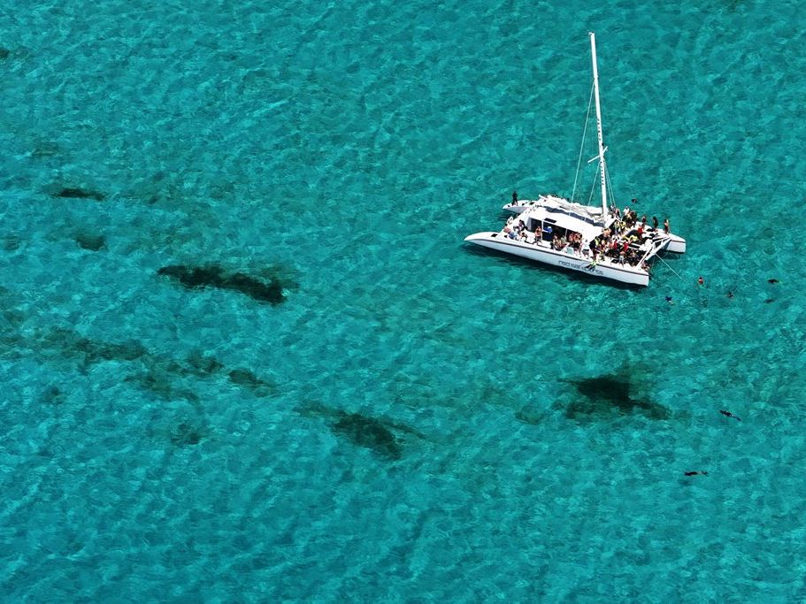 Catamaran anchored over pale sand with the shadows of stingrays visible in the water