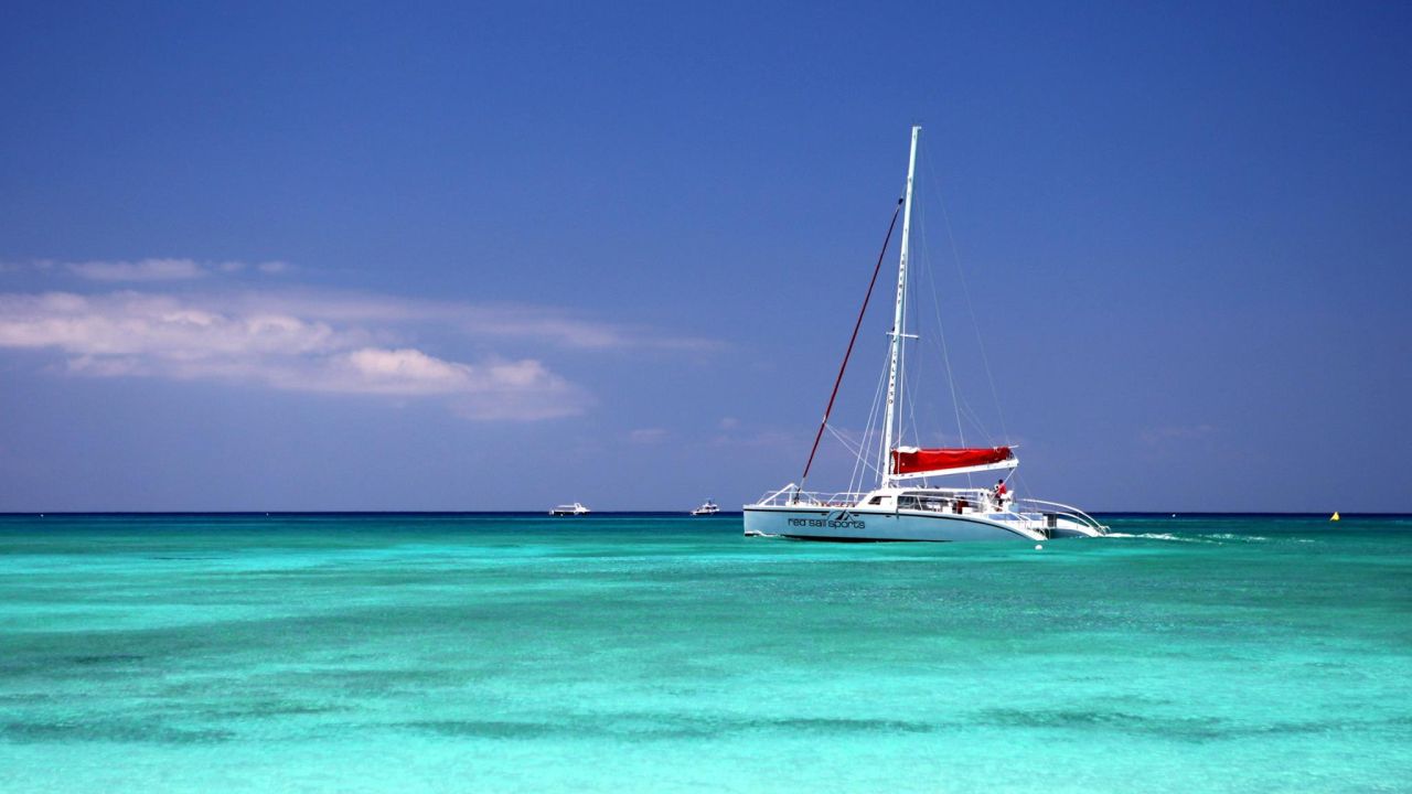 Sailing catamaran crossing calm turquoise water near shore under a deep blue sky