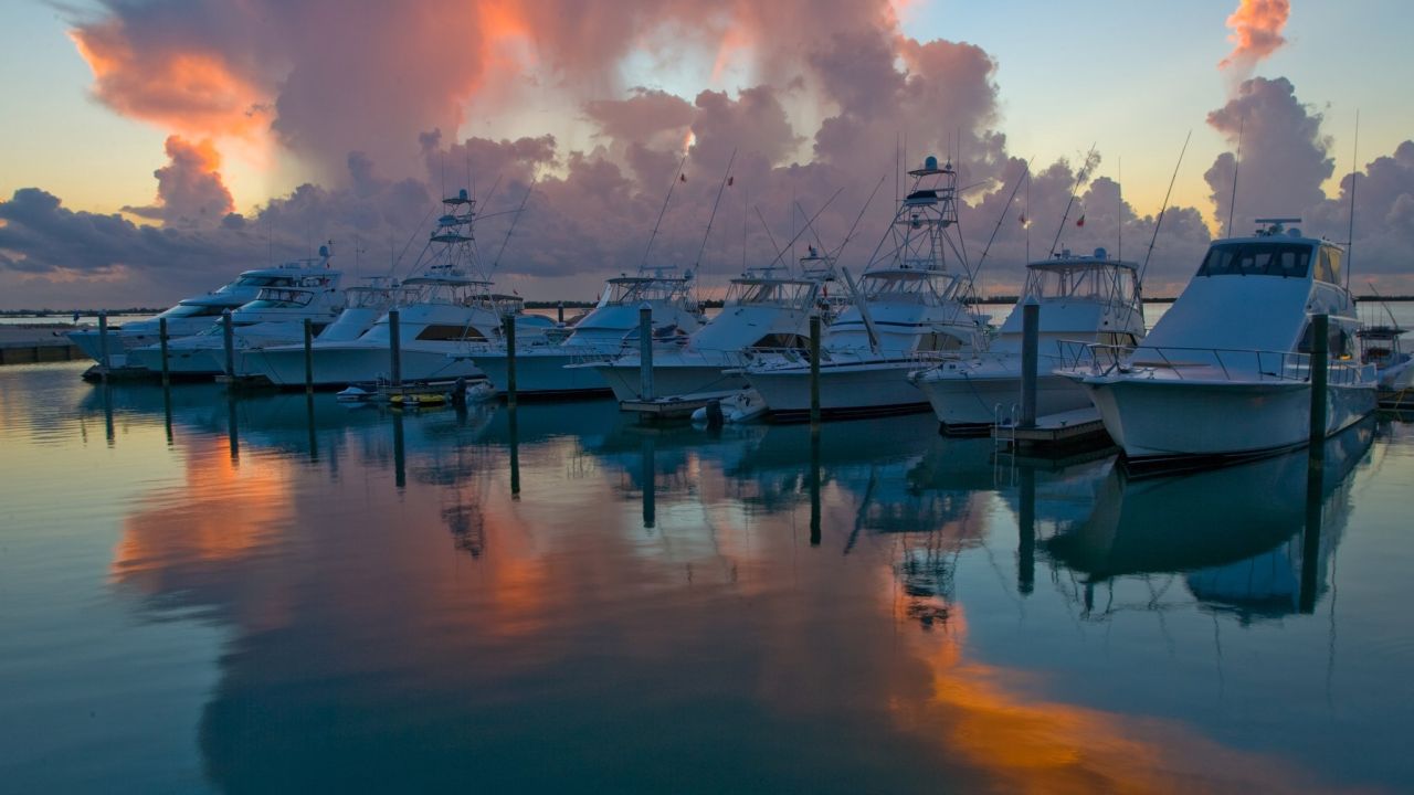 Sportfishing yachts berthed in a calm marina at sunset, with clouds reflected in the water