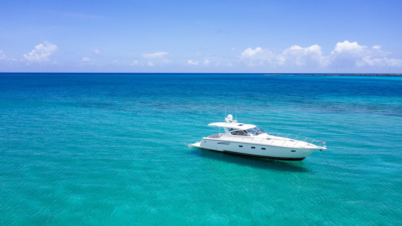 White motor yacht at anchor on open turquoise water under a blue sky with light clouds