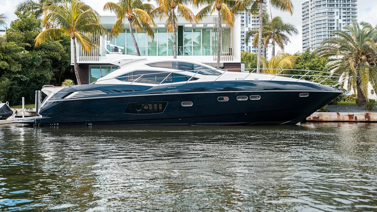Dark-hulled sport yacht moored beside a modern waterfront villa surrounded by palms