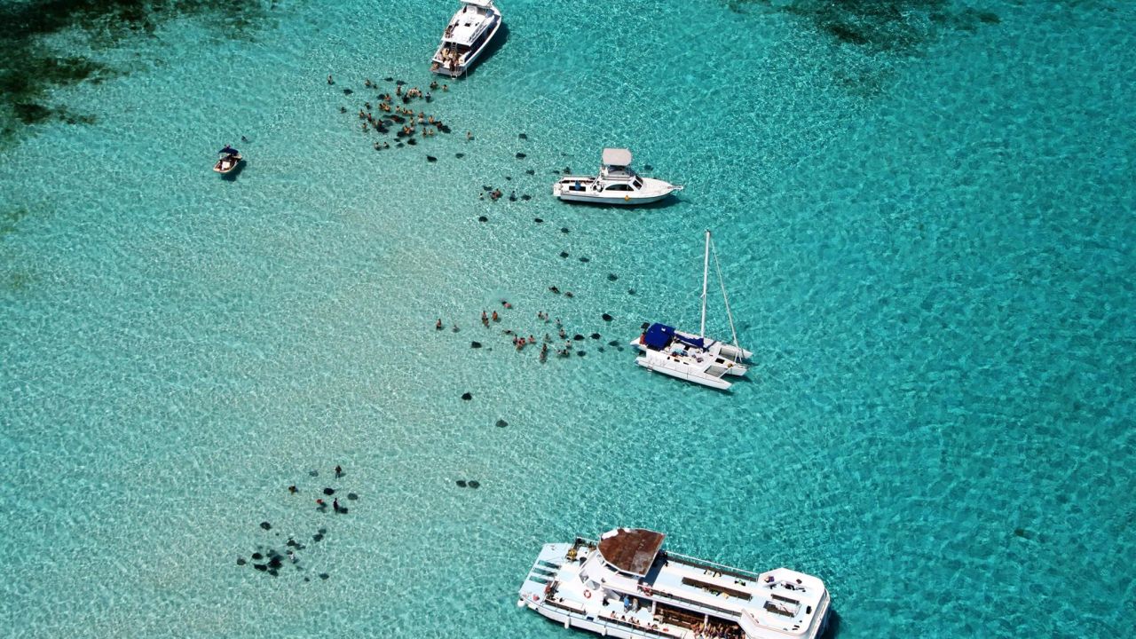 Aerial view of boats anchored over the shallow, sandy Stingray City Sandbar in Grand Cayman's North Sound, with stingrays visible in the water