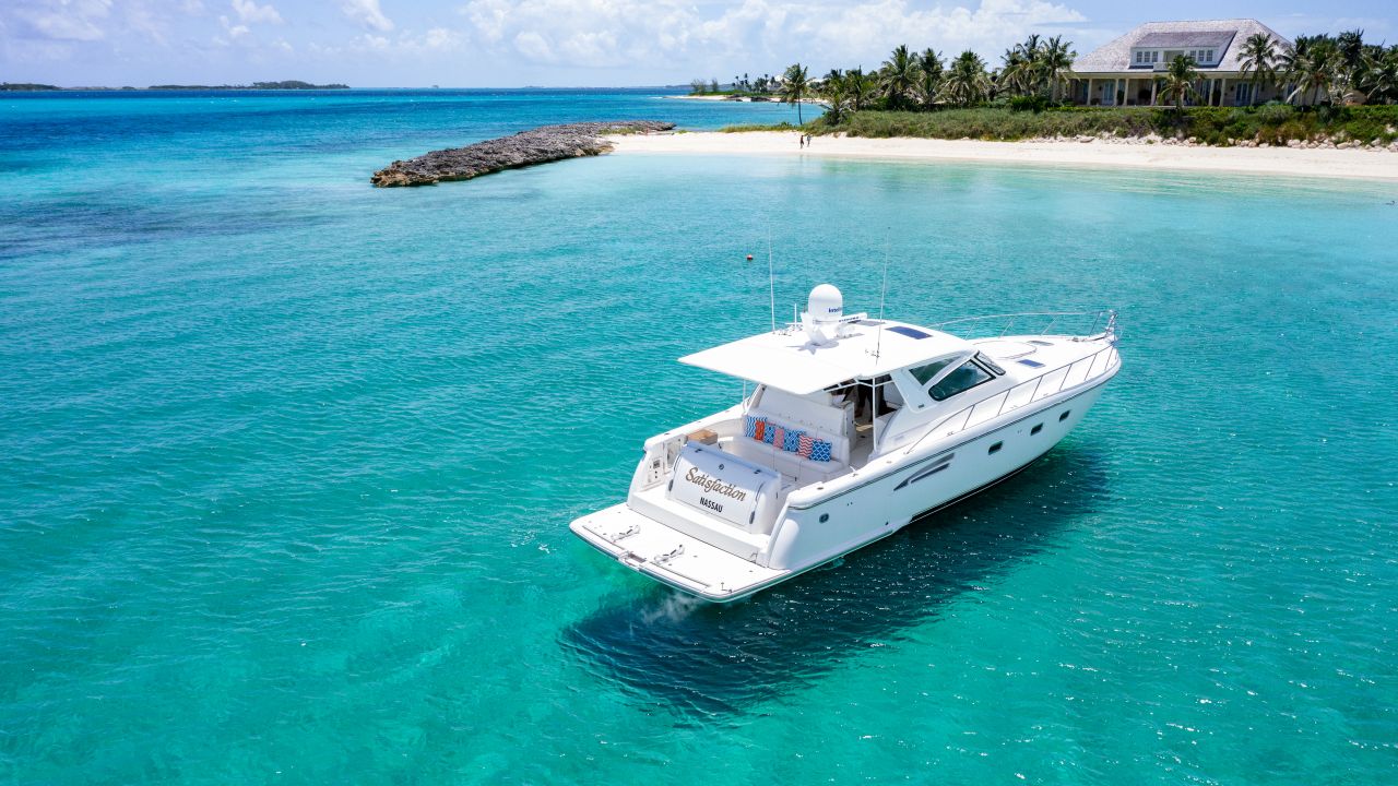 Aerial view of a white motor yacht anchored in clear water near a white-sand beach, rocky point and palm trees