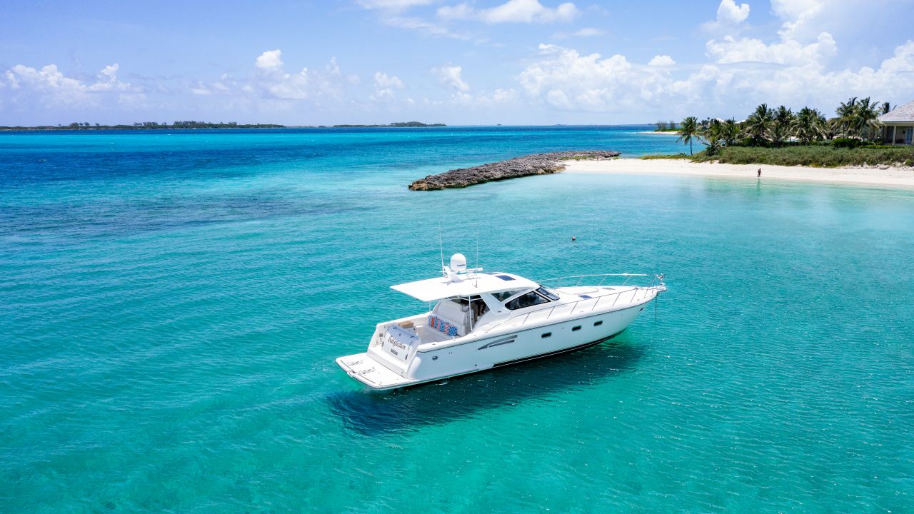 Aerial view of a white motor yacht anchored in clear turquoise water off a white-sand beach lined with palms