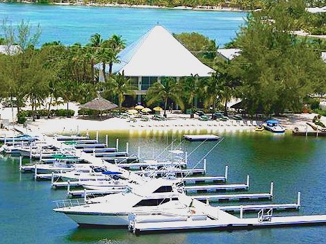 Boats moored along the docks of a marina at Cayman Kai, with a peaked roof and trees behind
