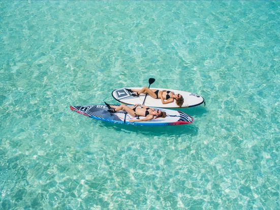 Two people relaxing on paddleboards in shallow turquoise water